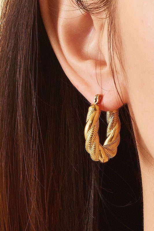Pair of gold twisted hoop earrings on a brown background