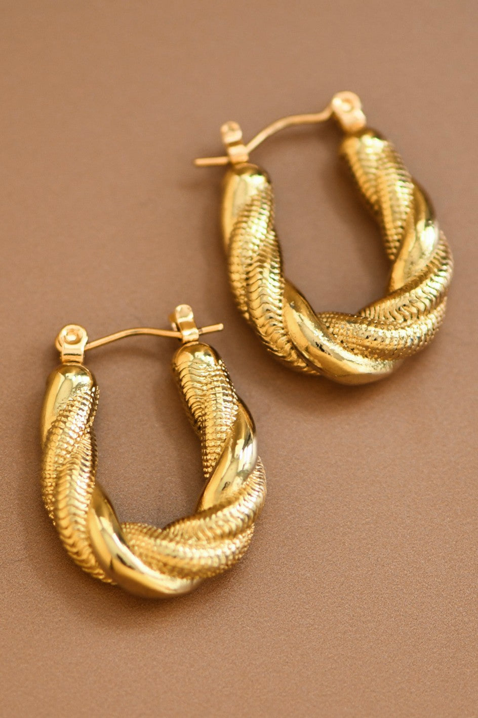 Pair of gold twisted hoop earrings on a brown background