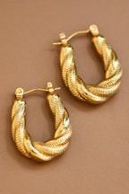 Pair of gold twisted hoop earrings on a brown background