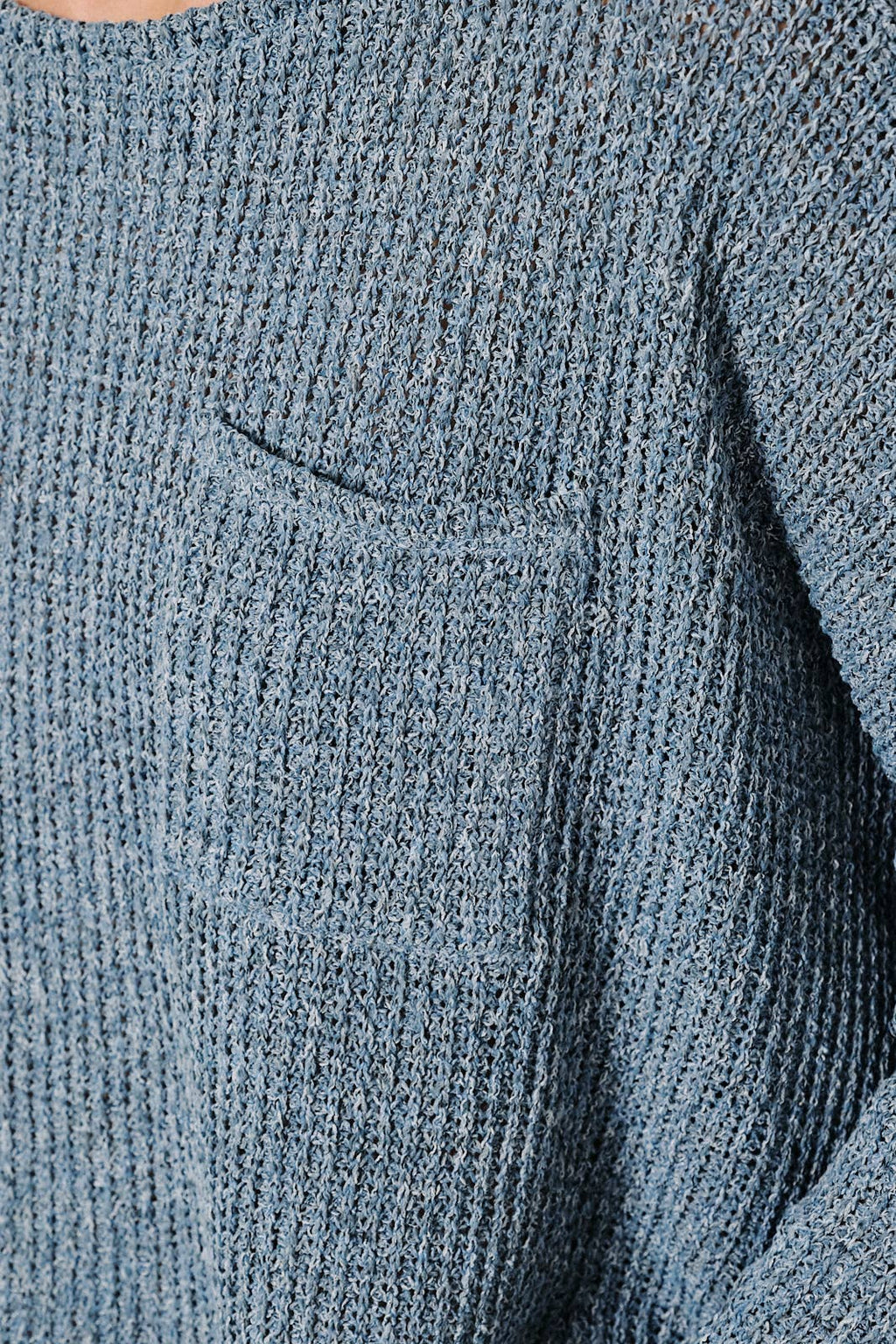 Close up of a textured denim blue long-sleeve knit sweater with pocket
