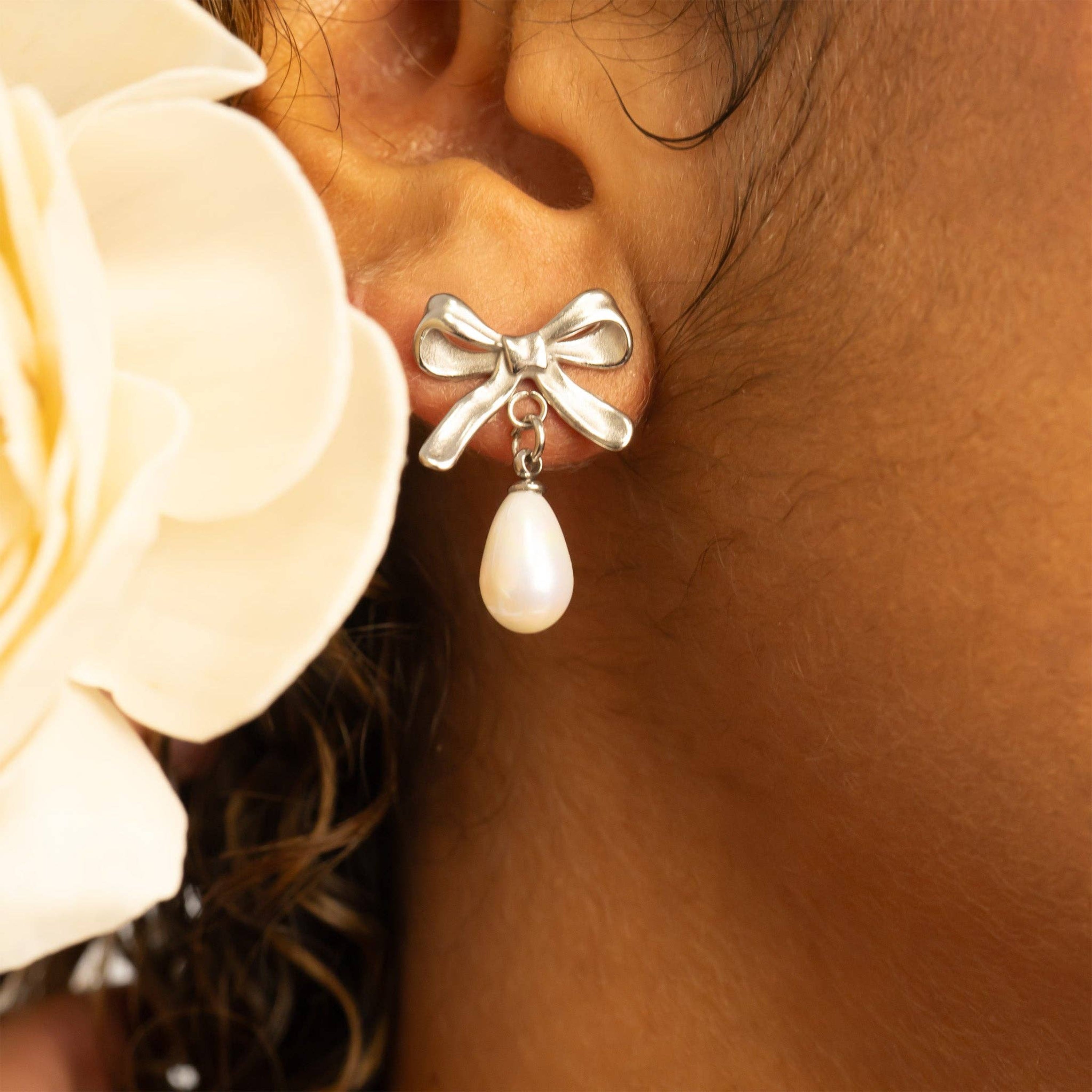 Woman wearing stainless steel bow-shaped earring with a freshwater pearl drop