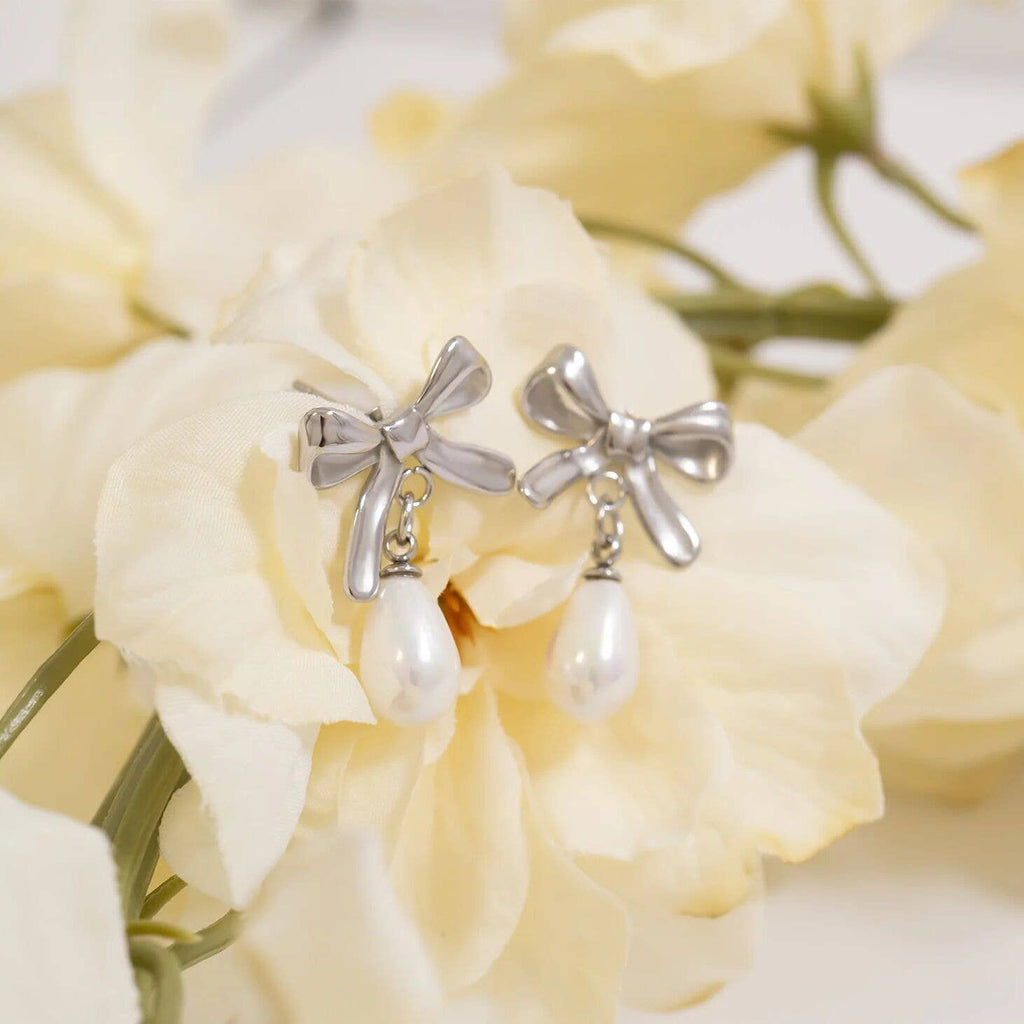 Silver bow-shaped earrings with freshwater pearl drops on a white flower background
