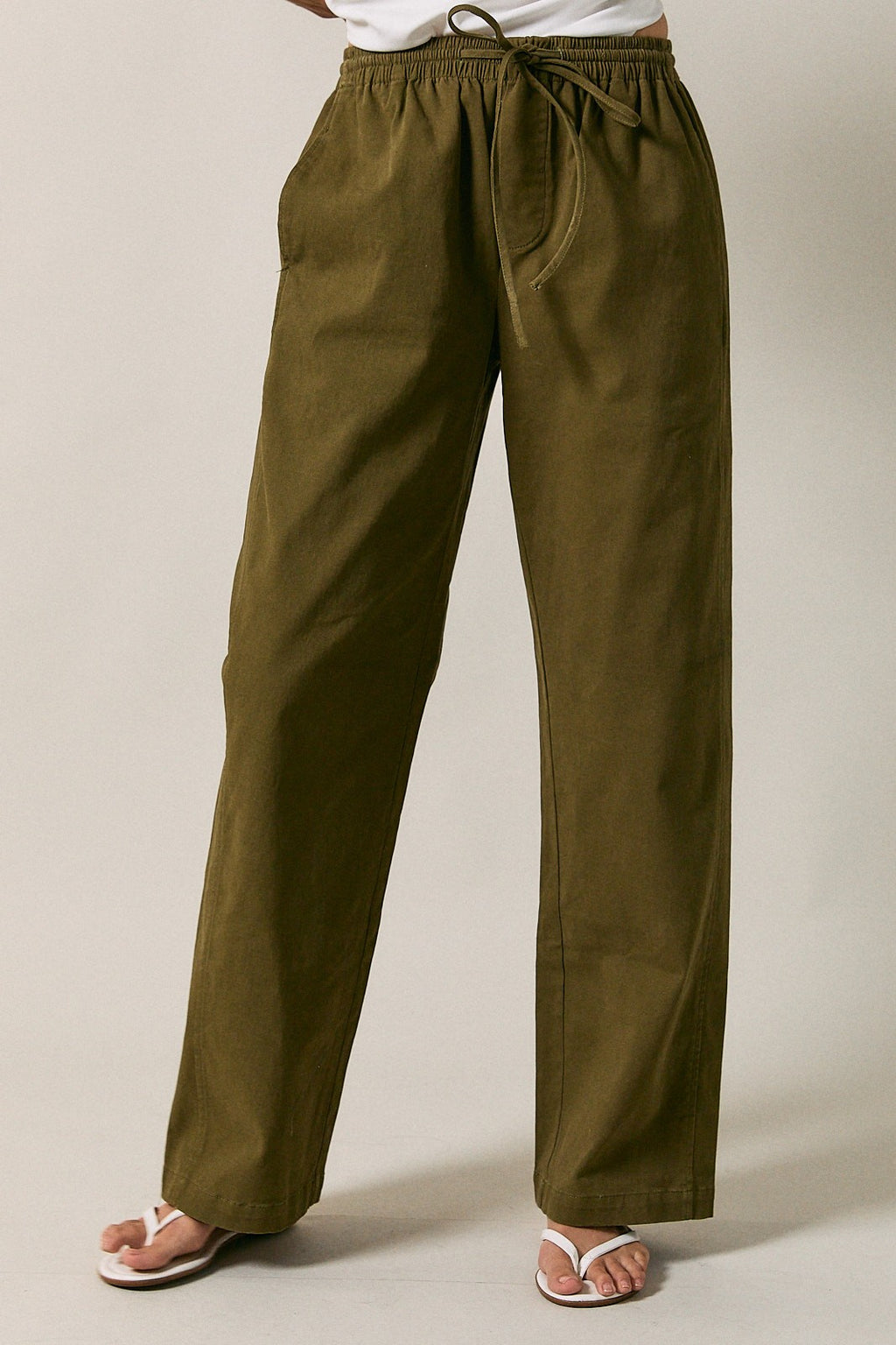 A woman modeling olive green straight-leg drawstring pants  standing against a solid beige studio background.