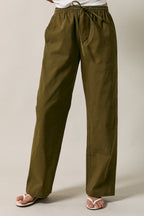 A woman modeling olive green straight-leg drawstring pants  standing against a solid beige studio background.