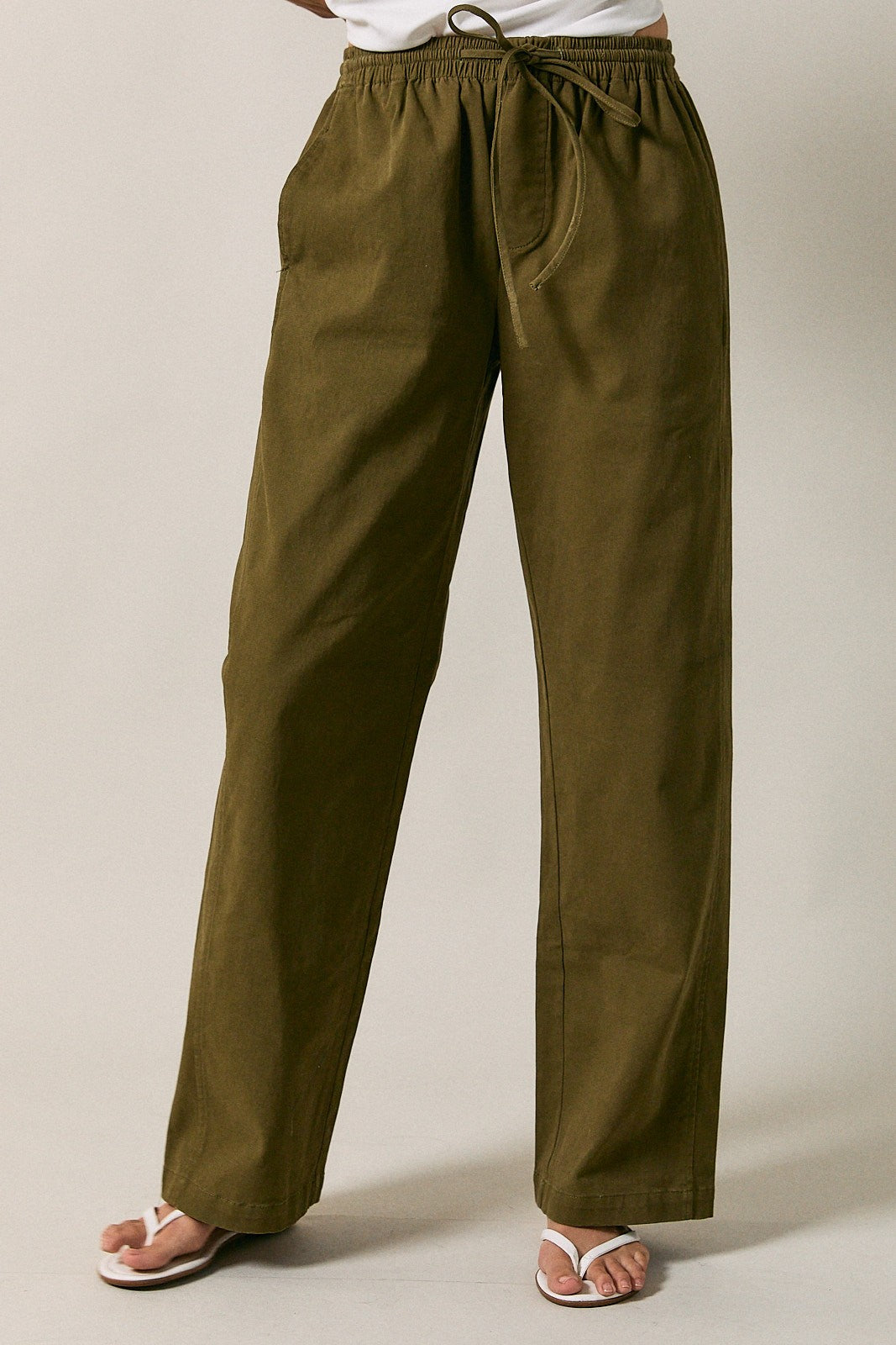 A woman modeling olive green straight-leg drawstring pants  standing against a solid beige studio background.