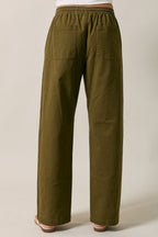 Back view of a woman modeling olive green straight-leg drawstring pants standing against a solid beige studio background.