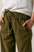 Close-up of a woman wearing olive green drawstring pants with side pockets, paired with a white top. 