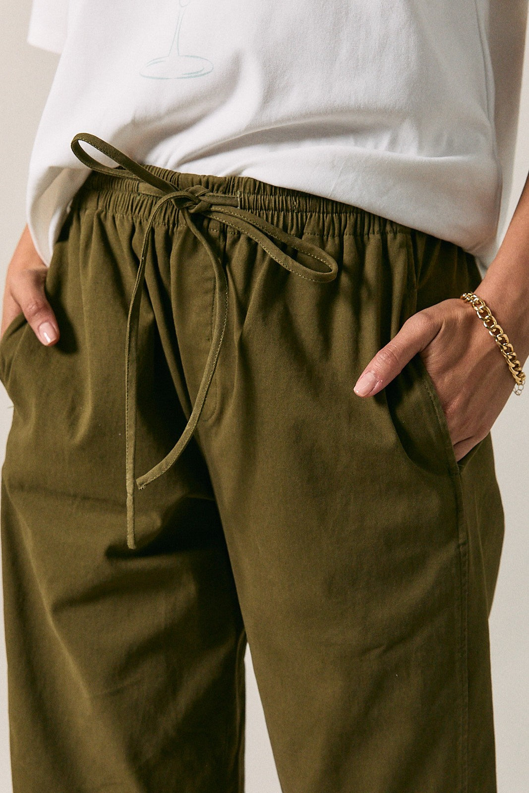 Close-up of a woman wearing olive green drawstring pants with side pockets, paired with a white top. 