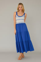 Woman wearing a cobalt maxi dress with a striped crochet top and tiered skirt in a minimalistic room.
