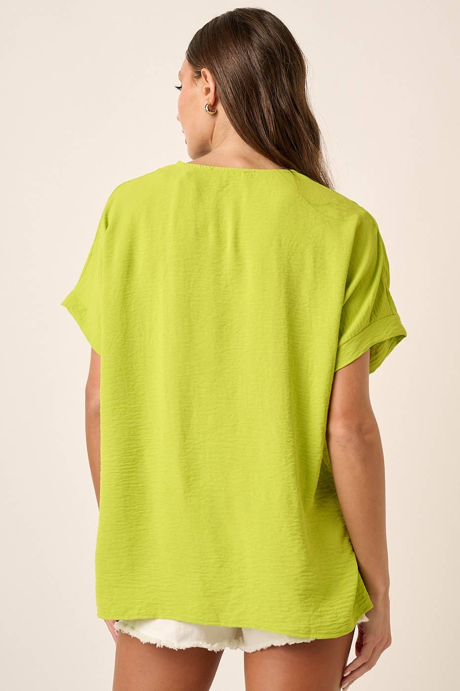 Back view of a woman wearing a lime top and white shorts on a beige background