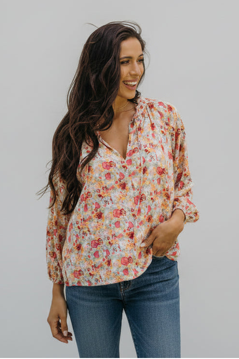 Woman wearing a floral blouse outdoors with greenery in the background