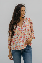 Woman wearing a floral blouse outdoors with greenery in the background