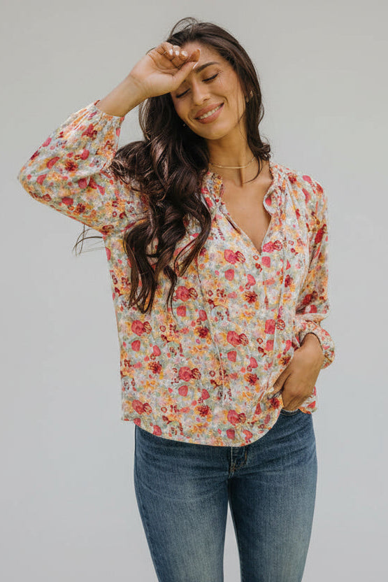 Woman wearing a floral blouse and jeans outdoors with greenery in the background