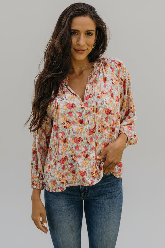 Woman wearing a floral blouse and jeans outdoors with greenery in the background