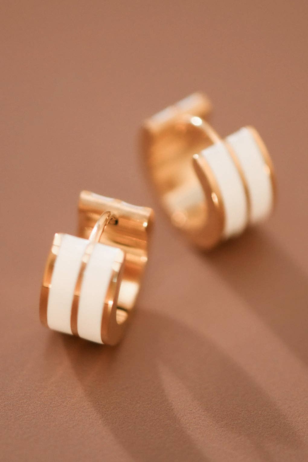 Gold tone and white enamel huggie hoop earrings on a brown background