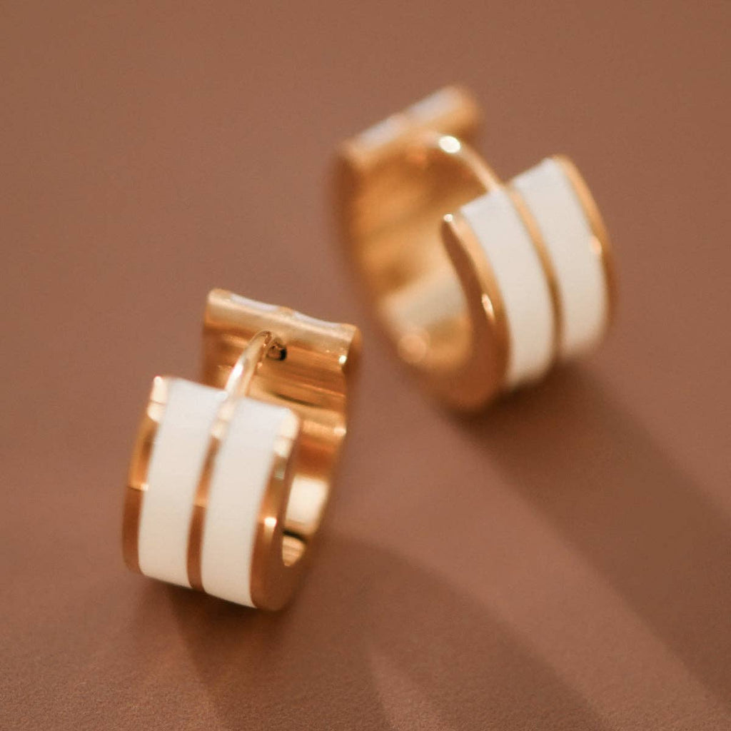 Gold tone and white enamel huggie hoop earrings on a brown background