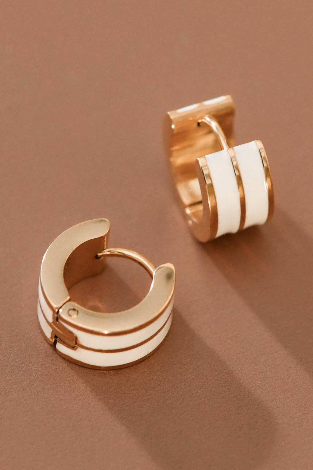 Gold tone and white enamel huggie hoop earrings on a brown background