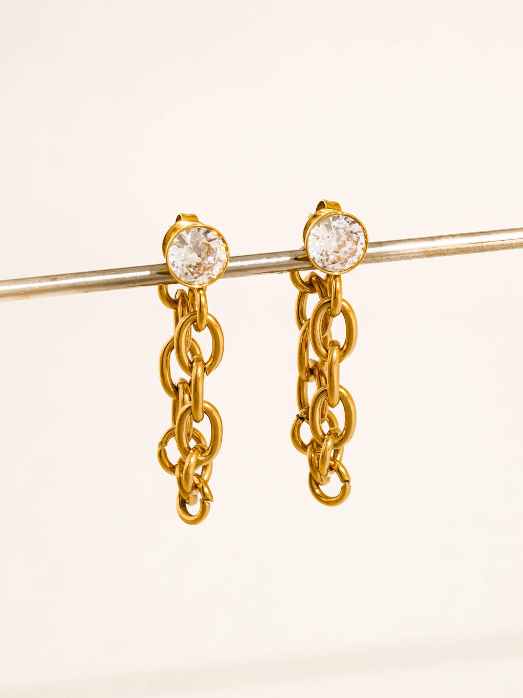Gold chain earrings with CZ stud on a beige background