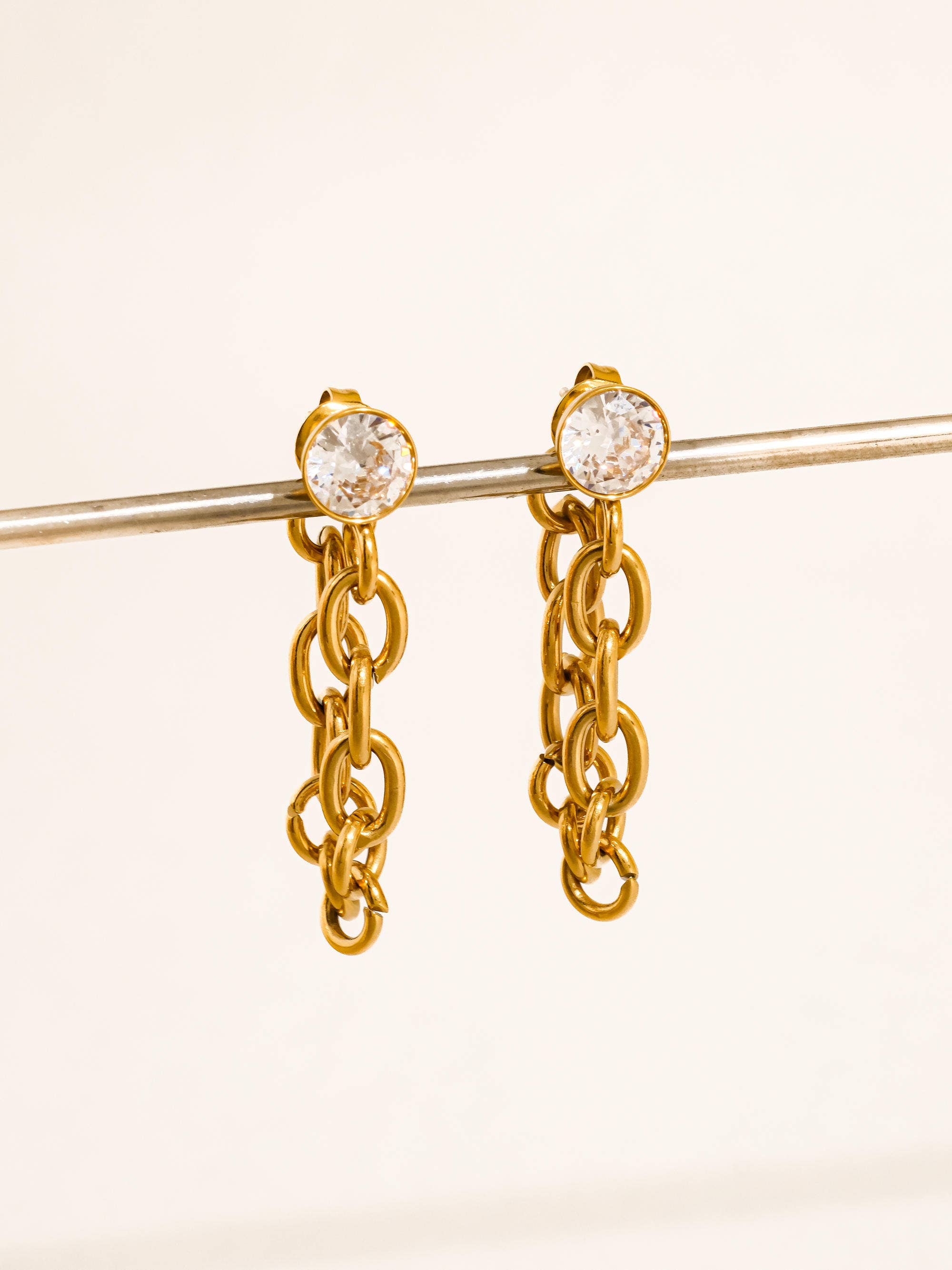 Gold chain earrings with CZ stud on a beige background