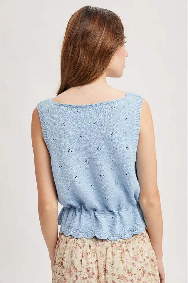 Back view of a woman wearing a sky blue sleeveless knitted tank top with scalloped hem on a plain background