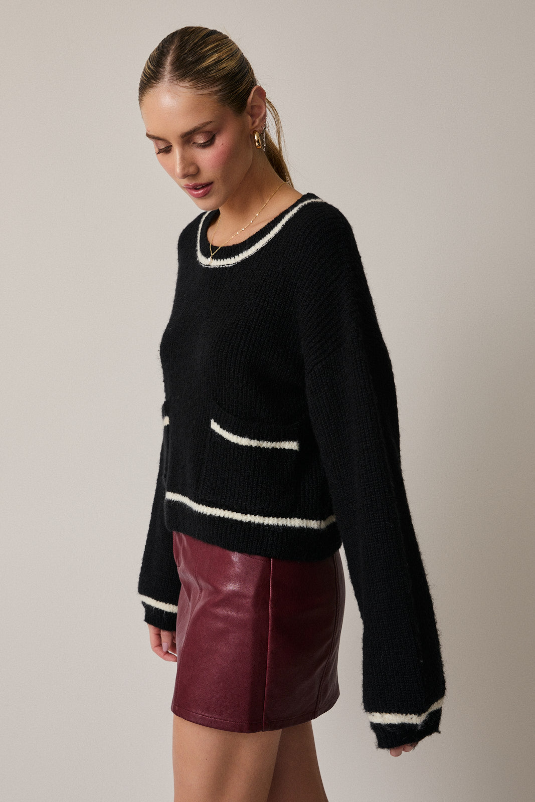 Woman wearing a black sweater with cream trim and a red leather skirt on a plain background