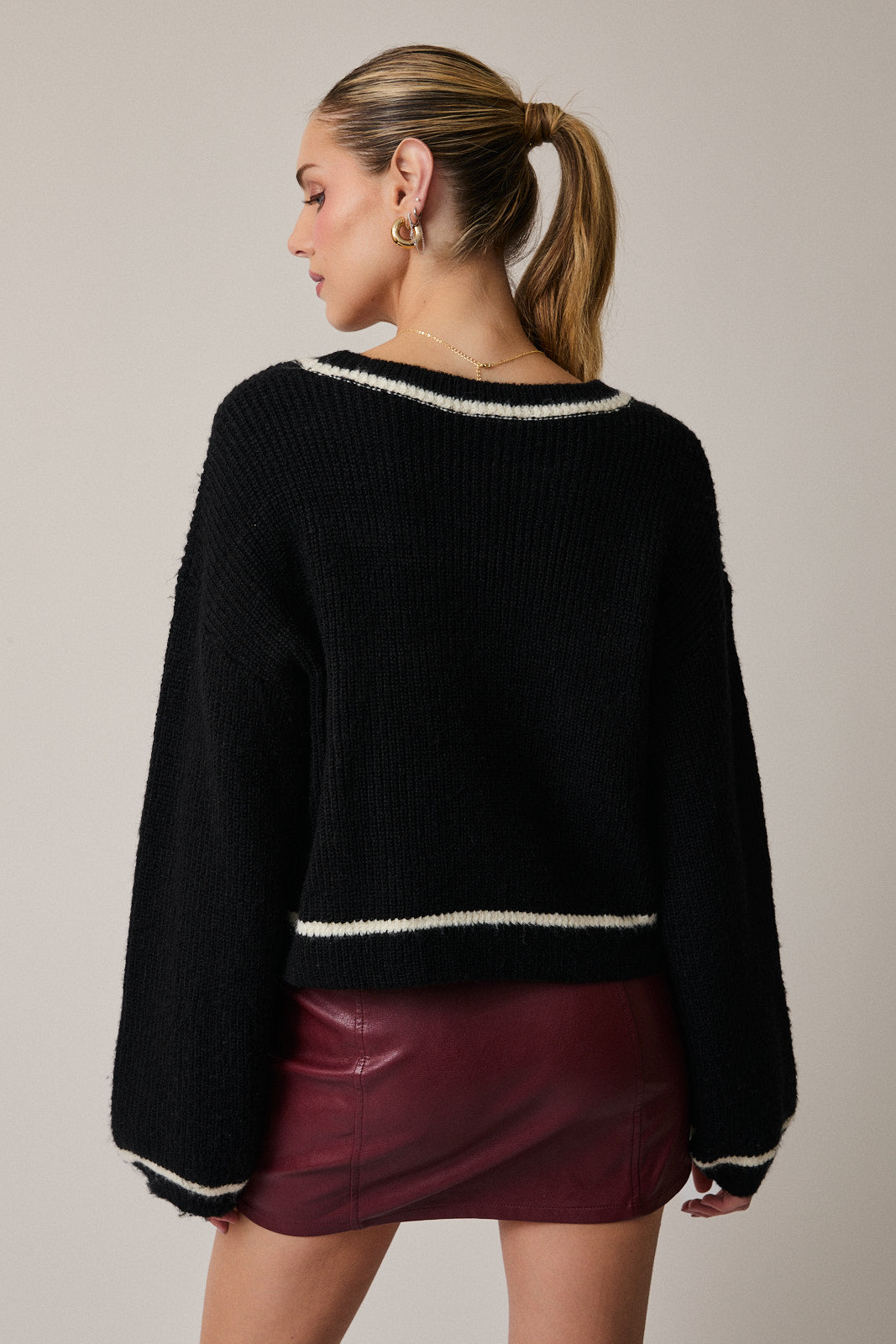 Woman showing the back of a black sweater with cream trim and a maroon skirt on a neutral background