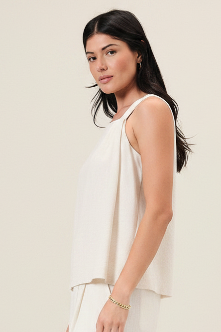 Woman wearing a natural linen blend sleeveless top with one side pleat detail against a white background