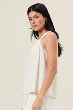 Woman wearing a natural linen blend sleeveless top with one side pleat detail against a white background