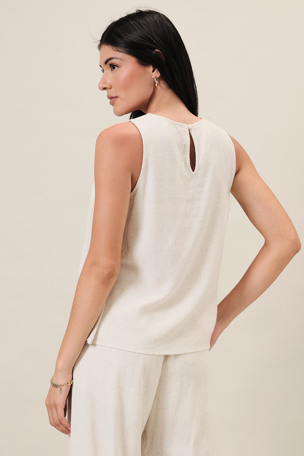 Back view of a woman wearing a natural linen blend sleeveless top  against a white background