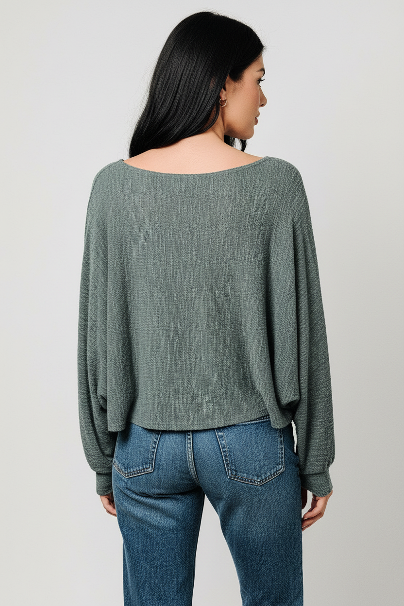 Back view of a woman shown from the back wearing a heather hunter green long-sleeve top and blue jeans against a light gray studio background.