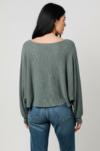 Back view of a woman shown from the back wearing a heather hunter green long-sleeve top and blue jeans against a light gray studio background.