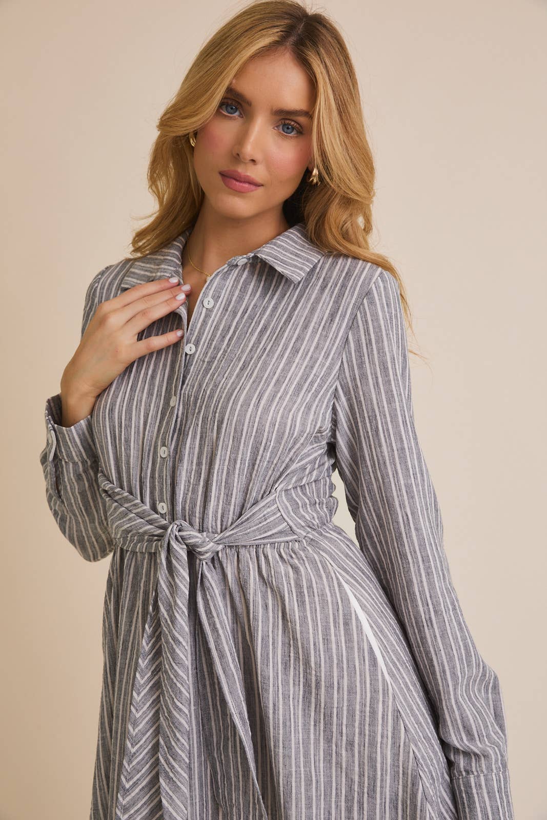 Woman wearing a blue and white striped shirt dress against a beige background