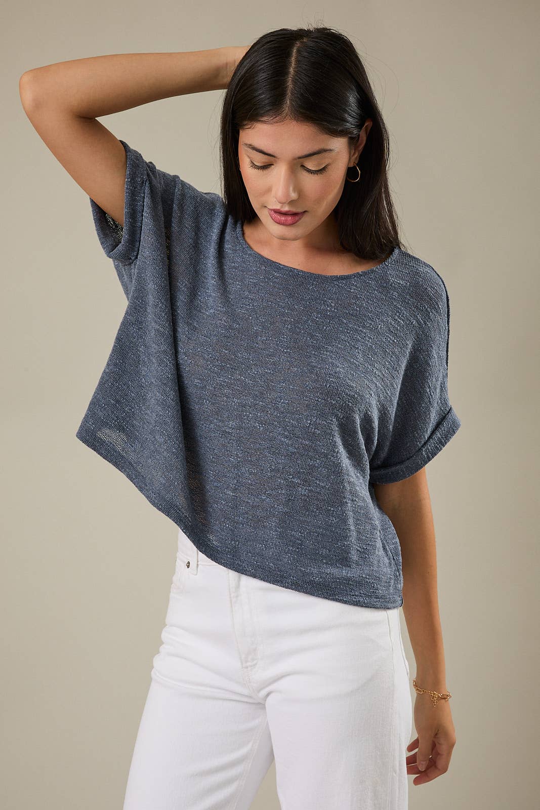 Woman wearing an indigo knit top and white pants against a beige background