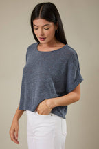 Woman wearing an indigo knit top and white pants against a beige background