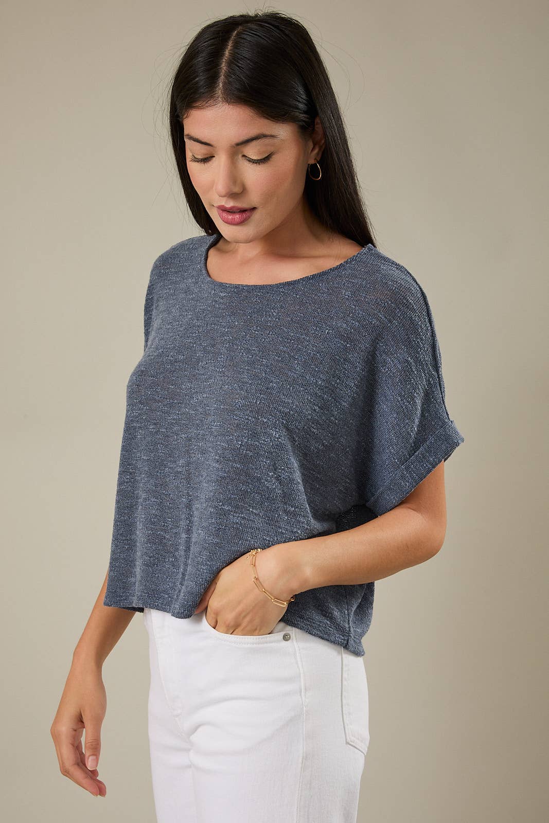 Woman wearing an indigo knit top and white pants against a beige background
