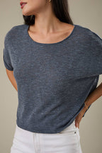 Woman wearing an indigo knit top and white pants against a beige background