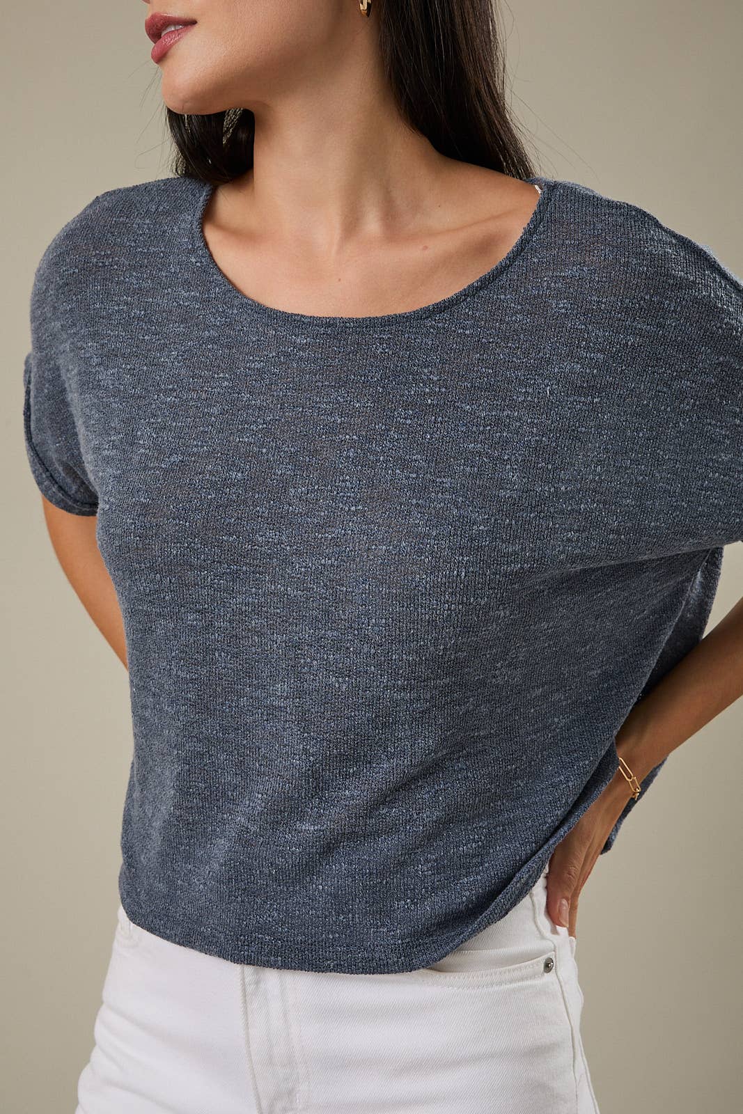 Woman wearing an indigo knit top and white pants against a beige background