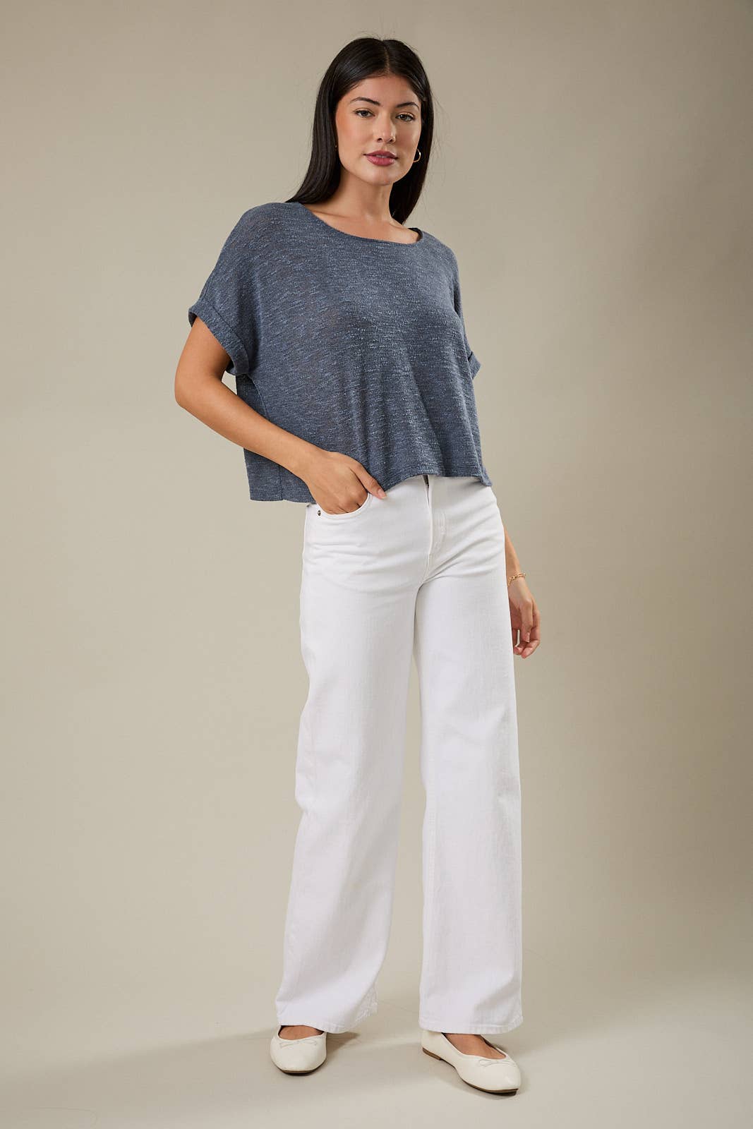 Woman wearing an indigo knit top and white pants against a beige background