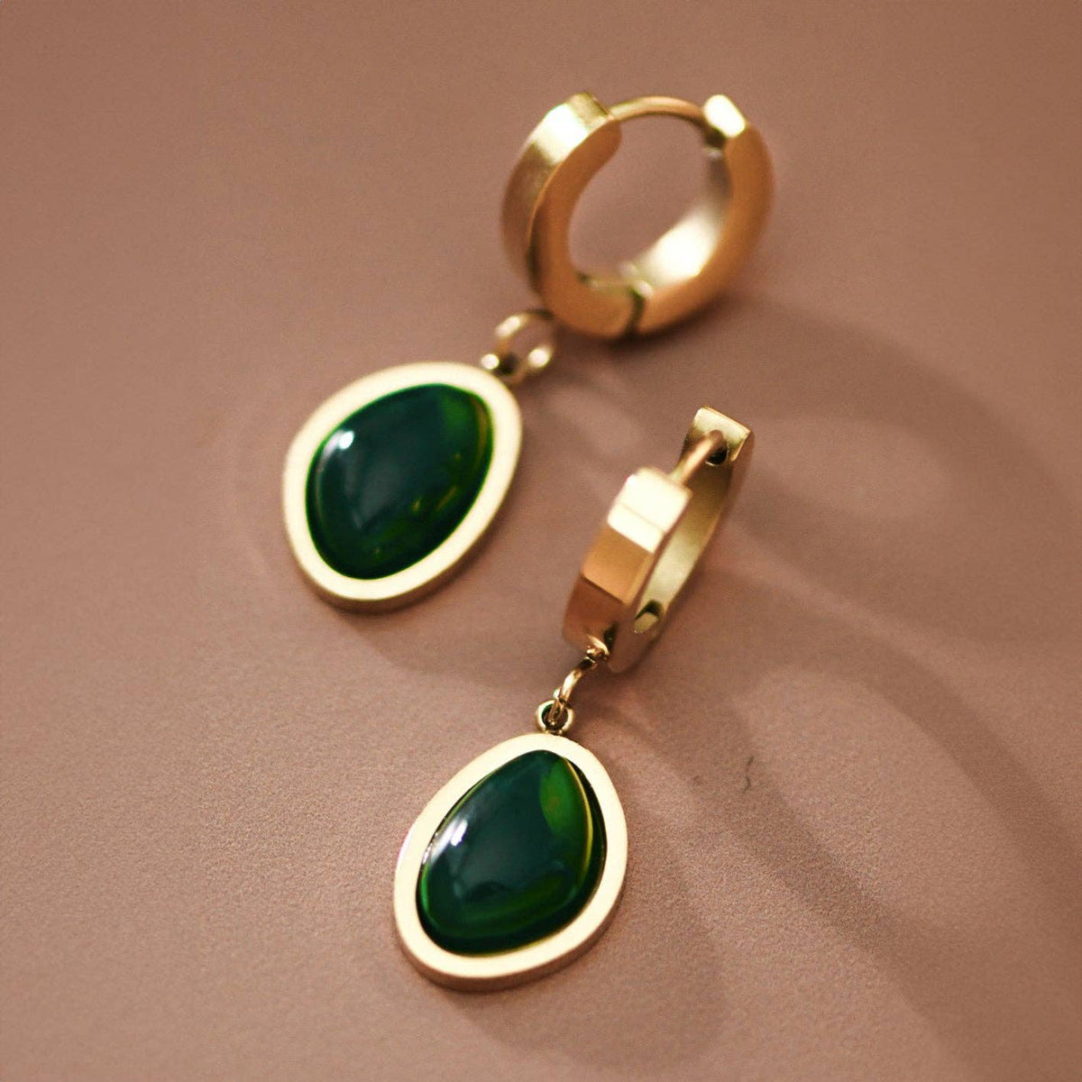Gold hoop earrings with green gemstones on a brown background