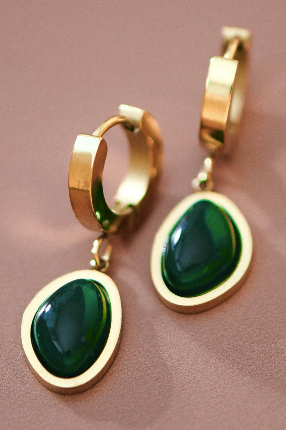 Gold hoop earrings with green gemstones on a brown background