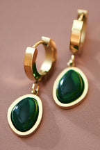 Gold hoop earrings with green gemstones on a brown background