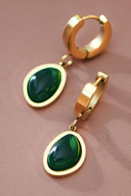 Gold hoop earrings with green gemstones on a pink background