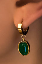 Gold earring with a green gemstone worn on an ear against a neutral background