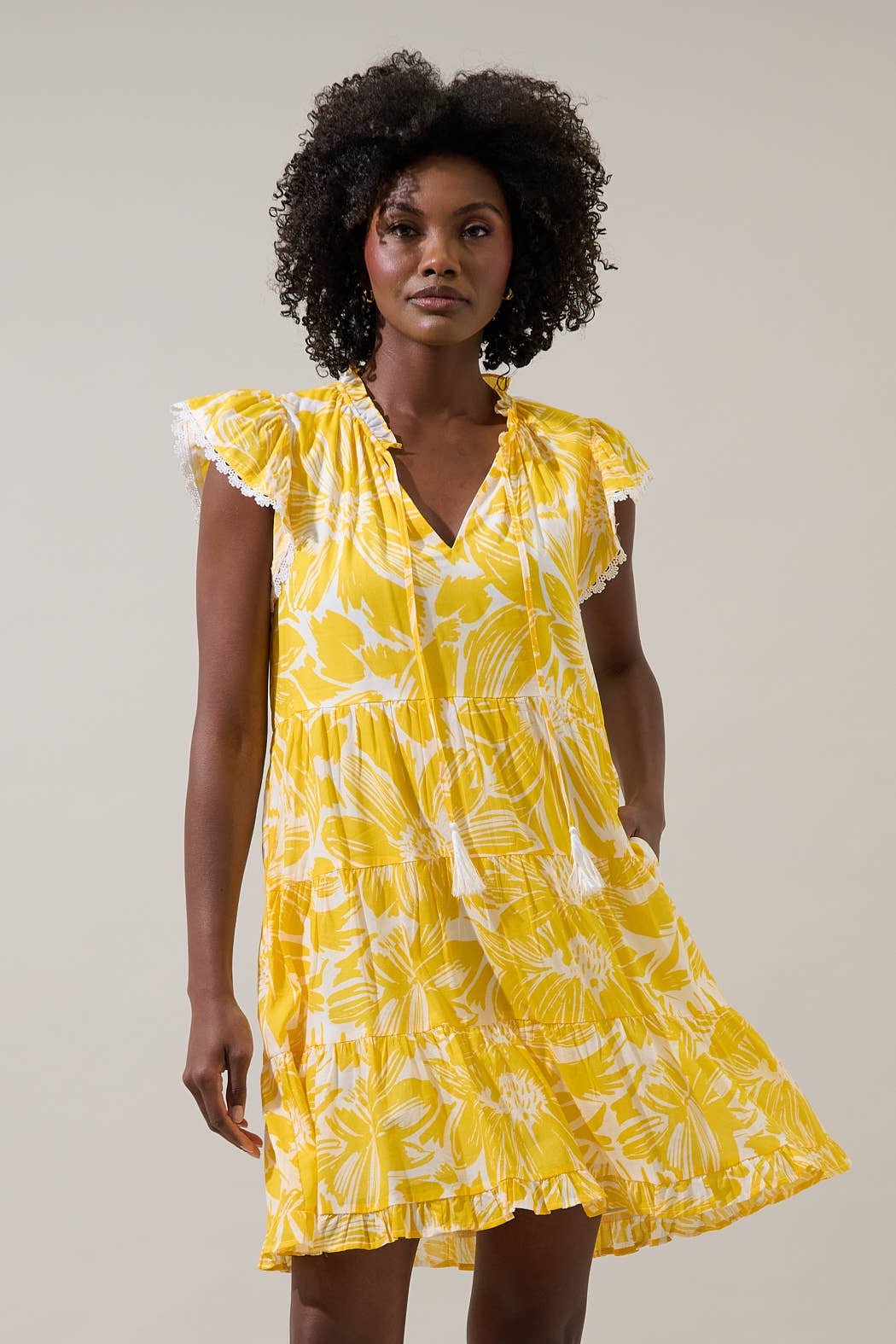 Woman wearing a yellow floral dress with flutter sleeves against a plain background