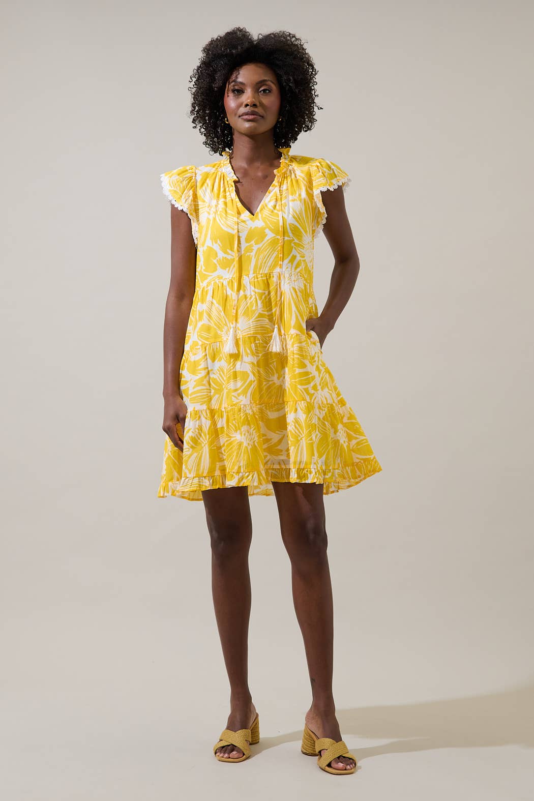 Woman wearing a yellow floral dress with flutter sleeves against a plain background