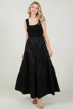 Woman wearing a black knit sleeveless tank maxi dress with poplin asymmetrical tiered skirt on a white background