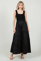 Woman wearing a black knit sleeveless tank maxi dress with poplin asymmetrical tiered skirt on a white background