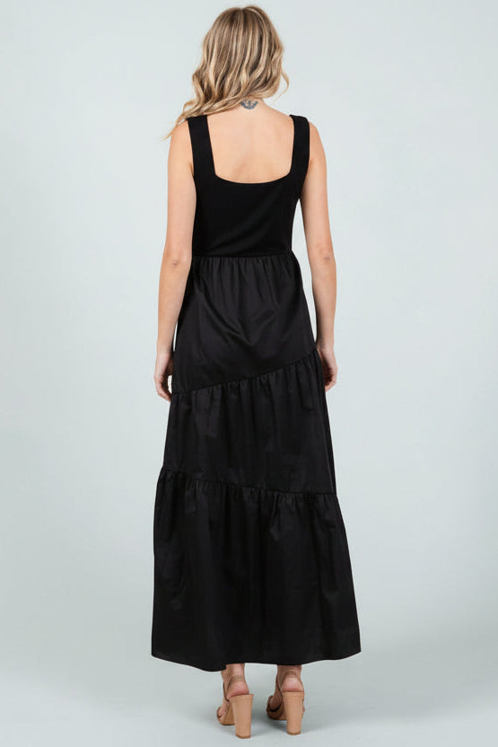 Back view of a woman wearing a black knit sleeveless tank maxi dress with poplin asymmetrical tiered skirt on a white background