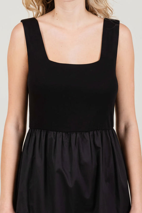 Close up of a woman wearing a black knit sleeveless tank maxi dress poplin skirt on a white background