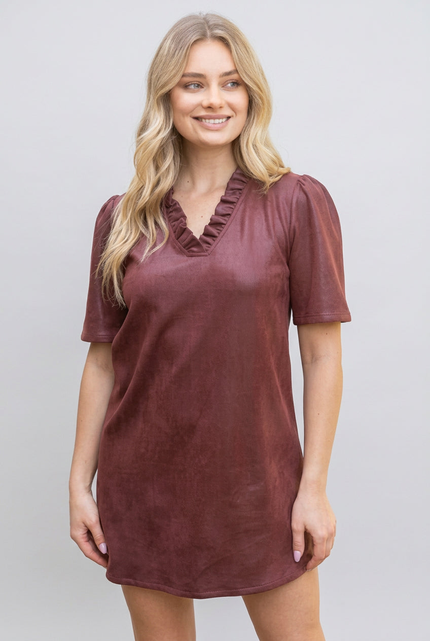 A woman modeling a short-sleeve, v-neck with ruffle dress in a burgundy faux leather fabric, set against a gray background